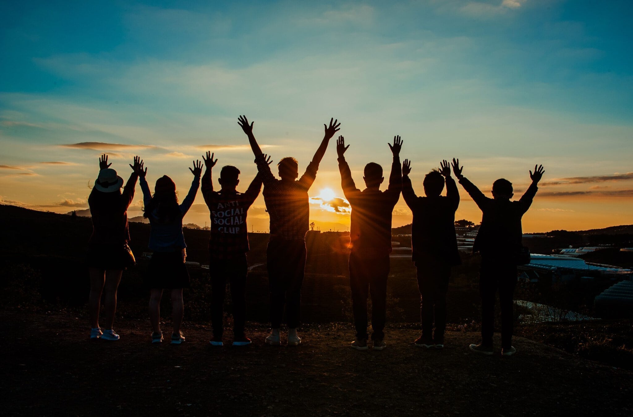A crowd celebrating on a beach at sunset with arms raised