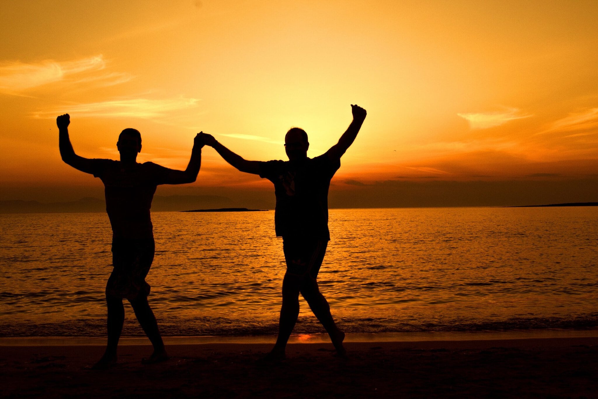 Silhouettes of people dancing on a beach at sunset