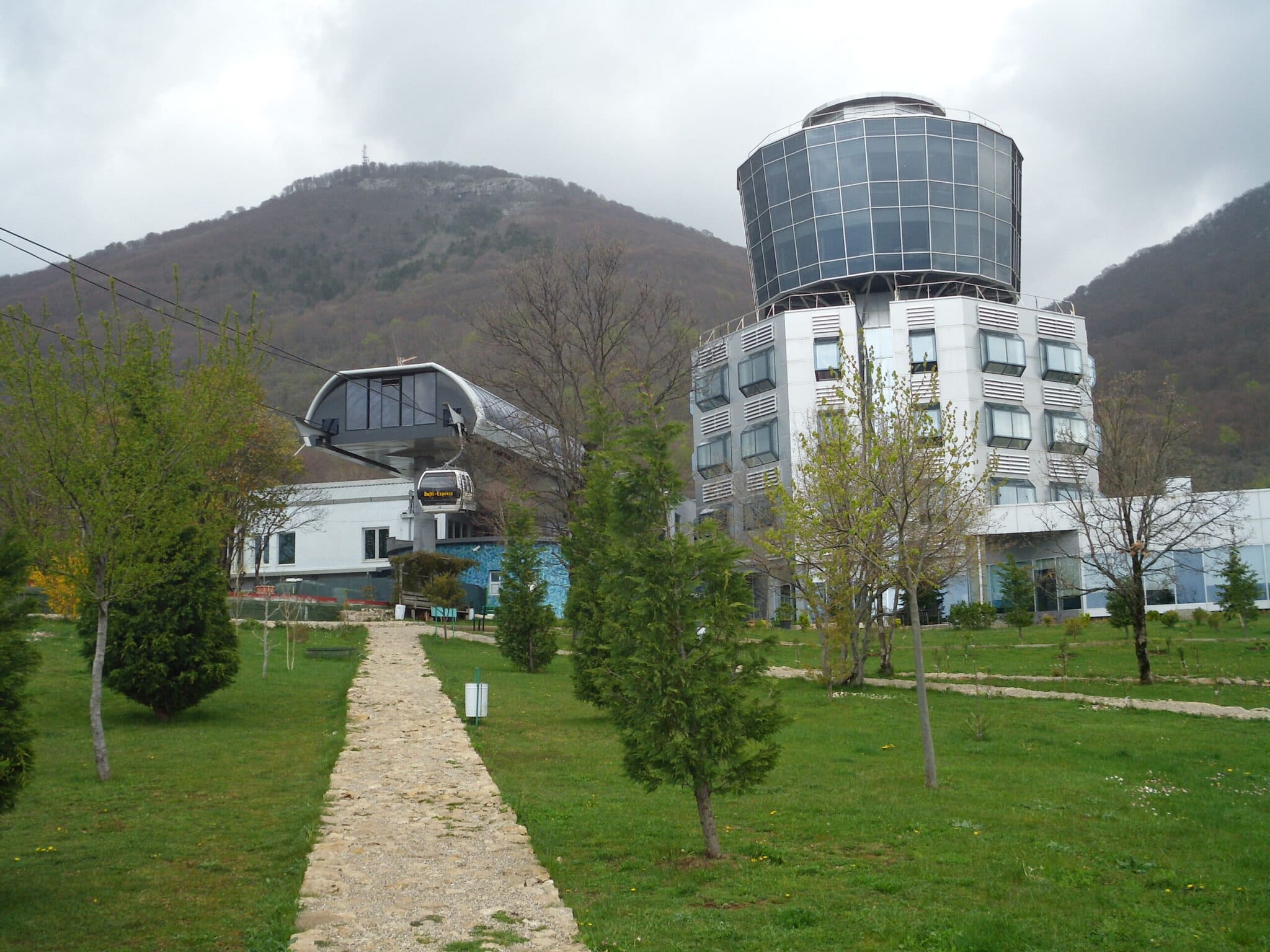 The Dajti Tower Belvedere Hotel, its rotating restaurant visible on top, with the Dajti Ekspres upper cable car station and a gondola arriving in front of it, and Mount Dajti's summit rising behind