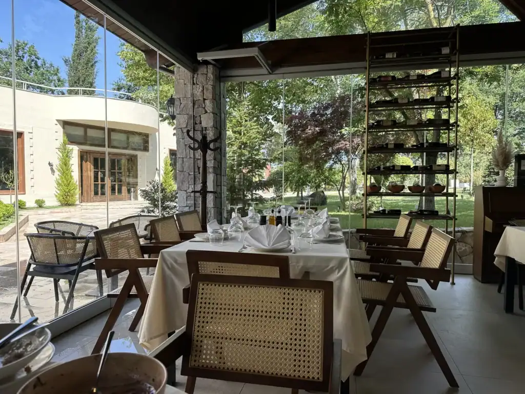 Glassed-in garden dining room at Farm 88, a farm-to-table restaurant near Tirana, with cane chairs and white linen