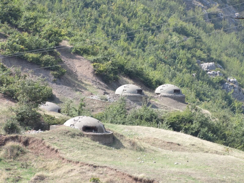 Four small mushroom-shaped concrete bunkers on a green Albanian hillside