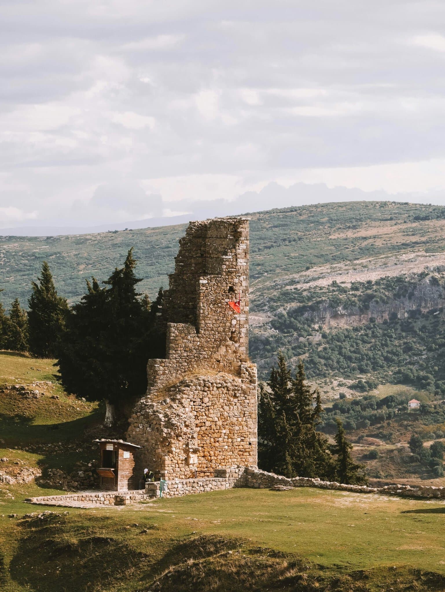 A stone fortification tower on a green hillside above Vlorë, Albania