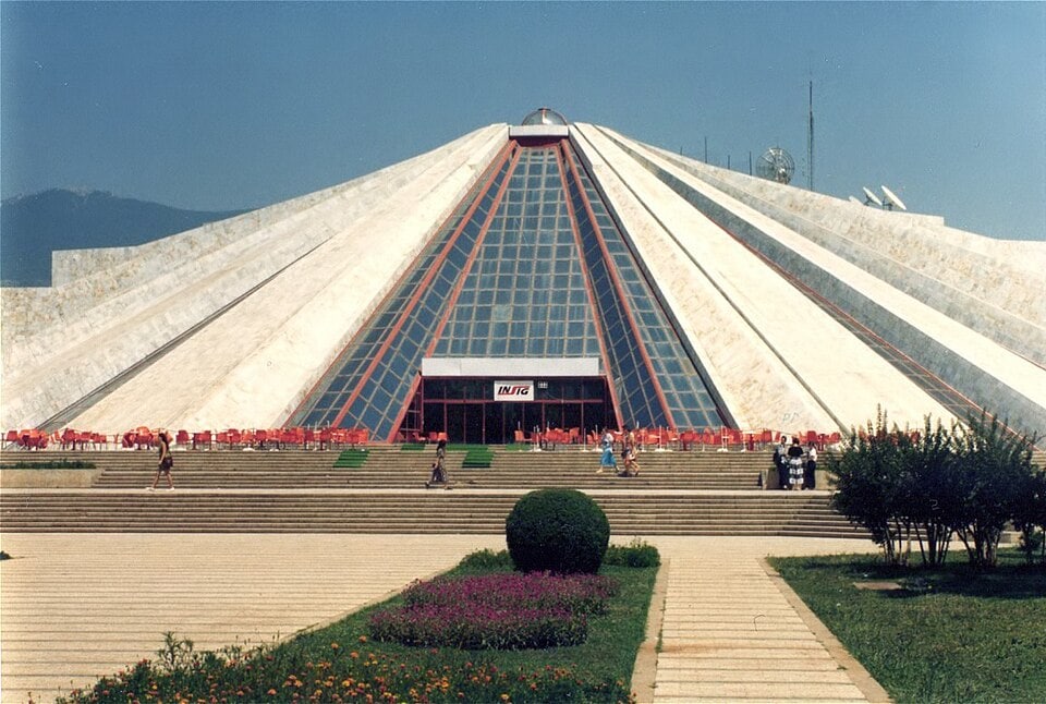 Black and white photograph from July 1996 of the Pyramid of Tirana, then still known as the Enver Hoxha Museum, seen from the street with its stepped white facade