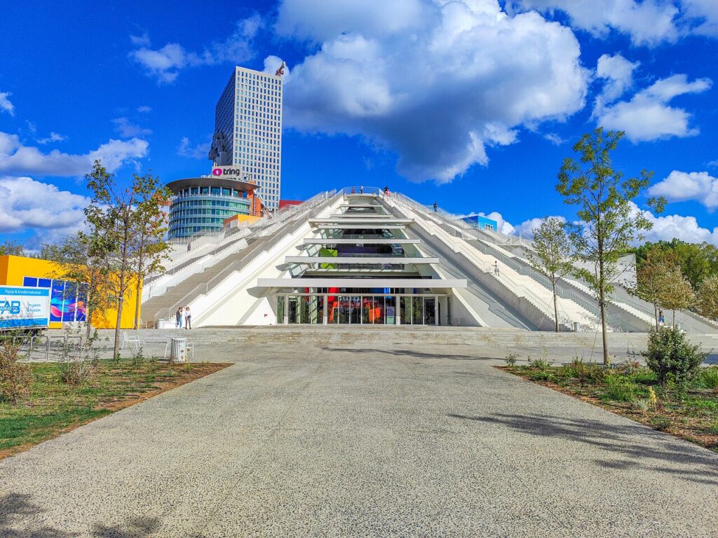 The renovated Pyramid of Tirana in October 2023, its stepped exterior and terraced roof rising over the boulevard with the European Trade Center and Downtown One towers behind it