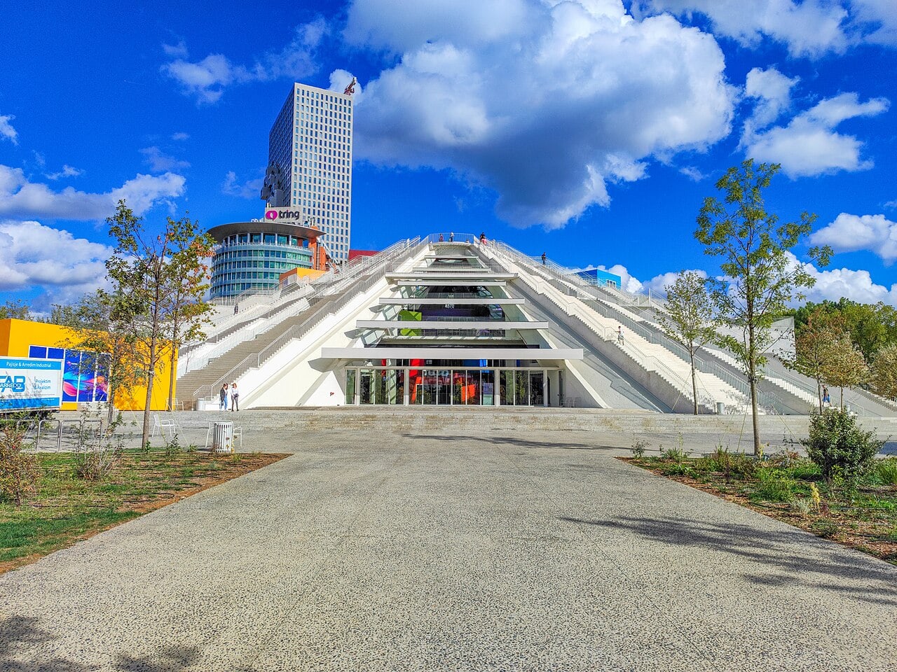 The renovated Pyramid of Tirana in October 2023, its stepped exterior and terraced roof rising over the boulevard with the European Trade Center and Downtown One towers behind it